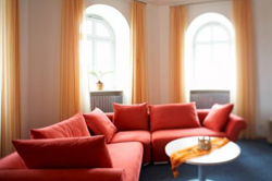 Das helle Zimmer ist mit 3 hohen Fenster mit Rundb�gen versehen. Lange gelbe Gardienen schm�cken es. Im Zimmer l�t ein rotes Sofa zum verweilen ein.